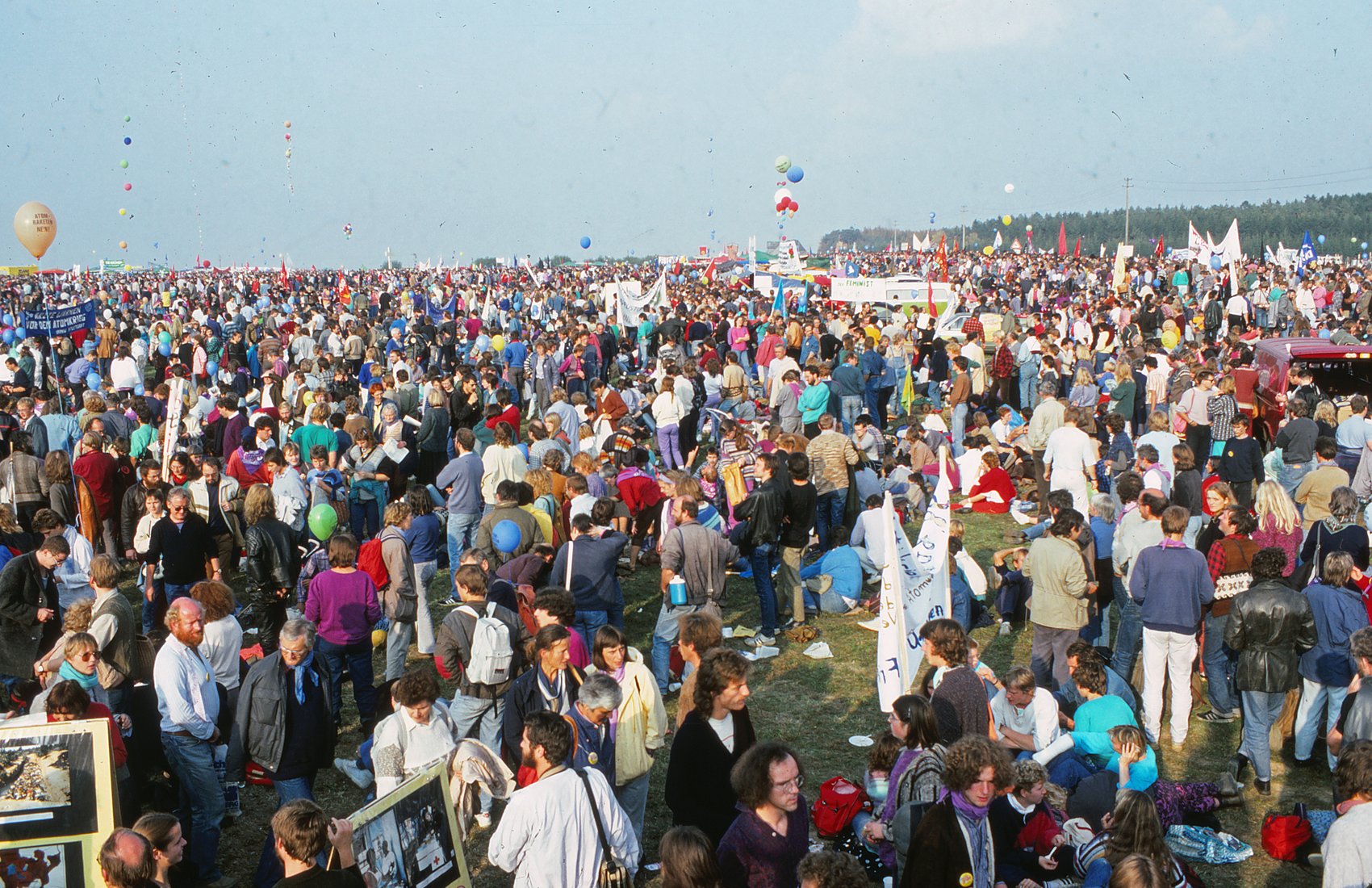 Weites Feld voller Menschen mit Transparenten und Luftballons bis zum Horizont