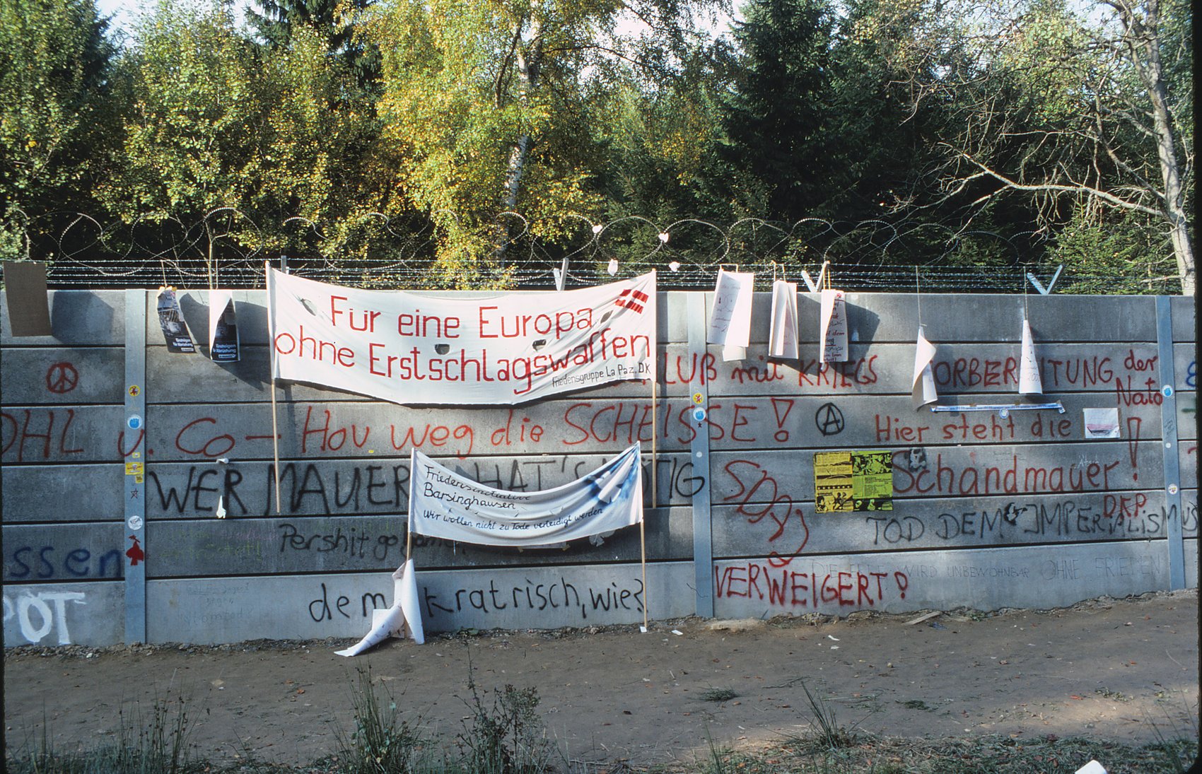 Mauer mit Transparenten und Aufschriften, darunter: Hier steht die Schandmauer